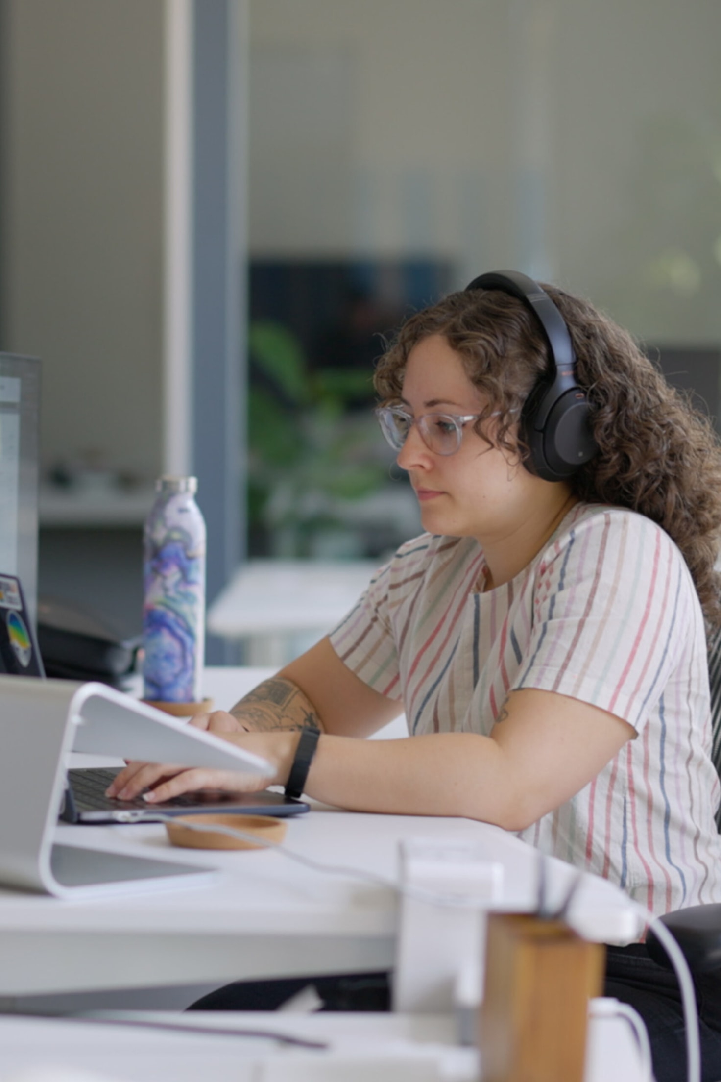 A full-stack engineer at Cuttlesoft deeply focused on development work, wearing noise-canceling headphones while working with both frontend and backend systems. Her workspace setup supports the demands of modern web development, where developers navigate between React components, API integrations, and database architecture. The scene captures the concentration required for full-stack development, where engineers seamlessly switch between Python, JavaScript, and cloud technologies. This focused development session shows how Cuttlesoft approaches complex software projects - with careful attention to both client-side experiences and server-side functionality.