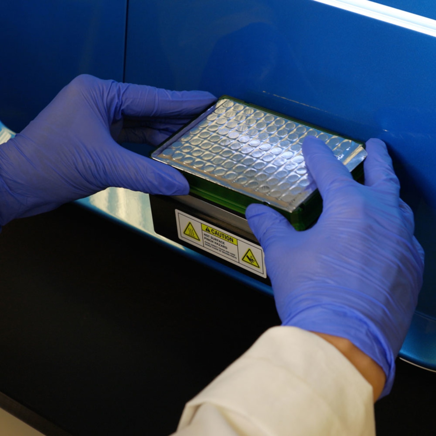 A lab technician loads a sample tray into the digital PCR continuum system for precise genetic analysis using custom Python software developed by Cuttlesoft.